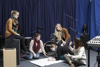 Dieses Bild zeigt eine Gruppe von weiblichen Studierenden umgeben von Instrumenten in einem Musikraum des Fachbereichs Sozial- und Kulturwissenschaften.